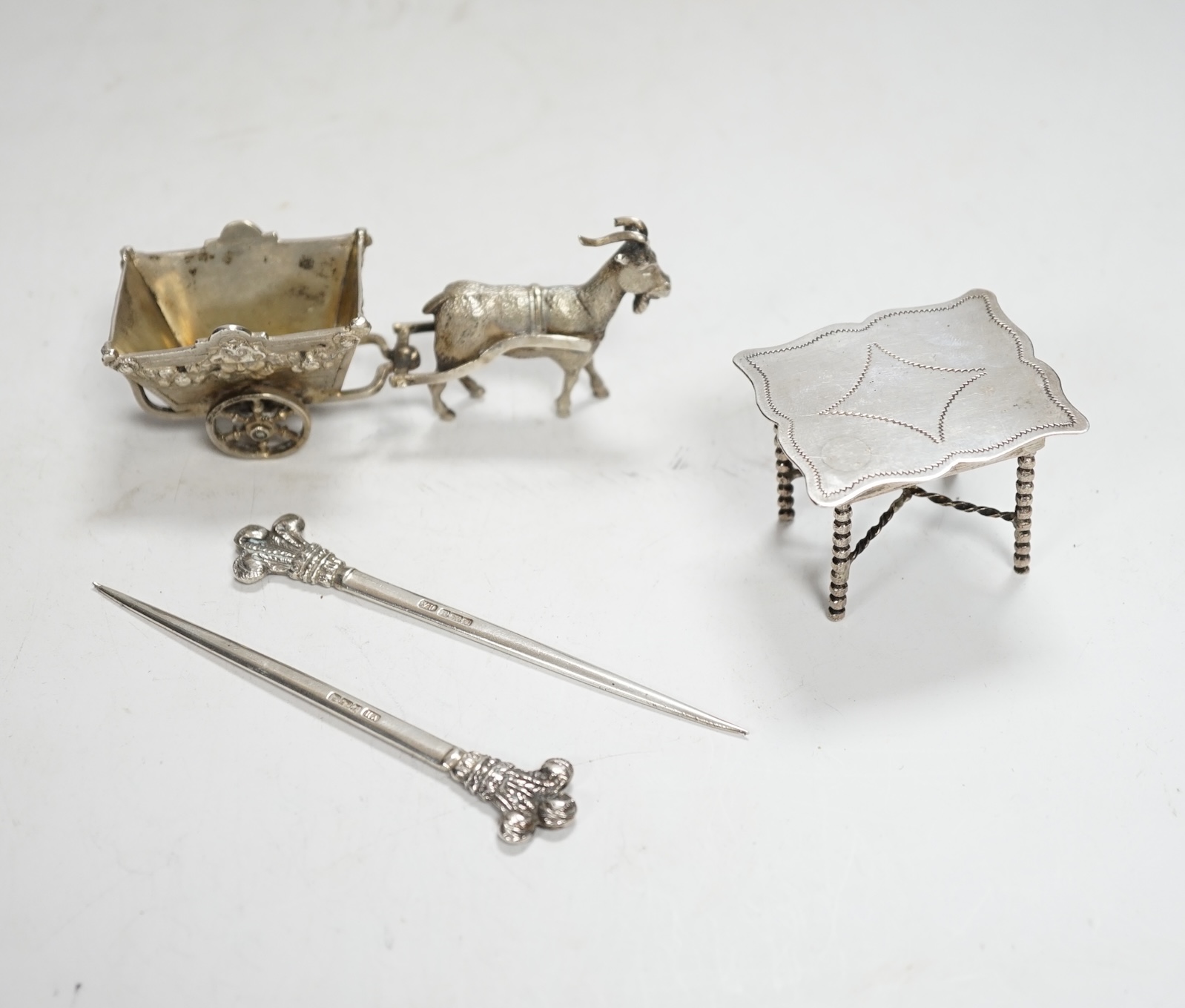 A pair of George V silver game skewers, with Prince of Wales feathers terminals, Atkin Brothers, Sheffield, 1915, 10.1cm, a Hanau? white metal miniature model of a goat pulling a cart and a Dutch white metal miniature mo